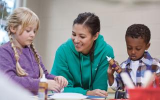 Two school age children making crafts with smiling counselor.