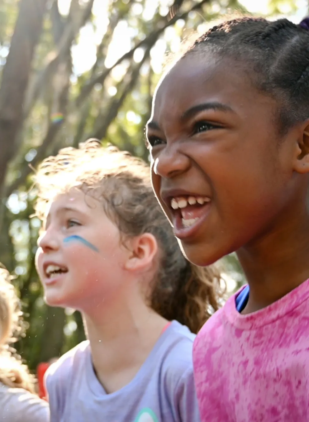 Four school age kids shouting a chant outside at camp. Sun peeks through the trees and shines their heads.
